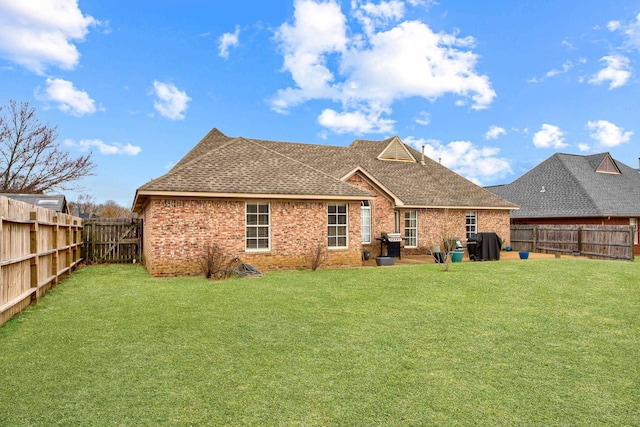 back of property with a lawn, brick siding, a fenced backyard, and a shingled roof