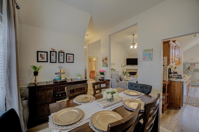 dining room with vaulted ceiling, a fireplace, light wood finished floors, and ceiling fan