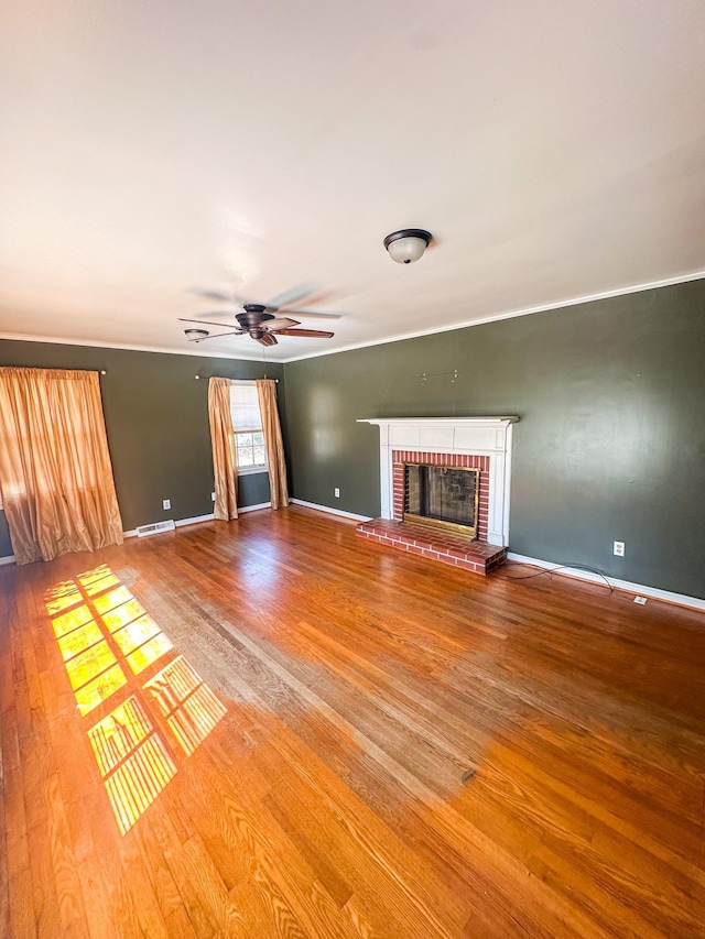 unfurnished living room featuring wood finished floors, visible vents, baseboards, ceiling fan, and a brick fireplace