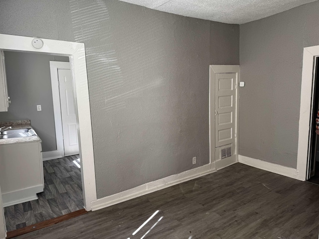 empty room featuring a sink, baseboards, a textured ceiling, and dark wood finished floors