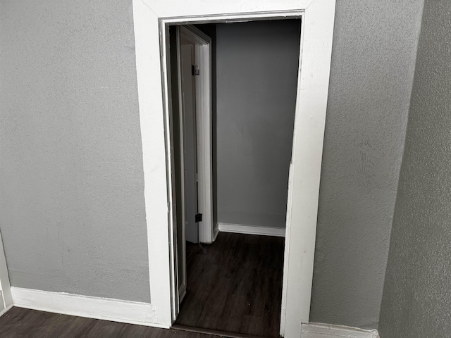 corridor featuring dark wood finished floors, a textured wall, and baseboards