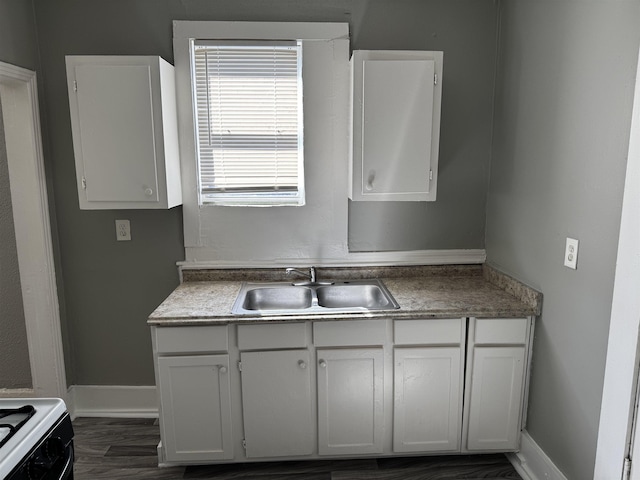 kitchen featuring a sink, baseboards, gas range, and white cabinetry