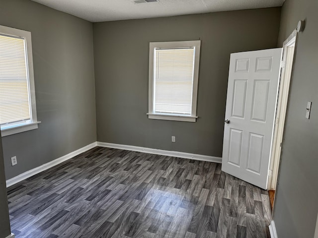 unfurnished room with dark wood finished floors, visible vents, and baseboards