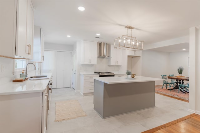 kitchen with a sink, white cabinetry, stainless steel range with gas cooktop, wall chimney exhaust hood, and light countertops