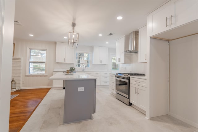 kitchen featuring light countertops, wall chimney range hood, white cabinets, and stainless steel gas range