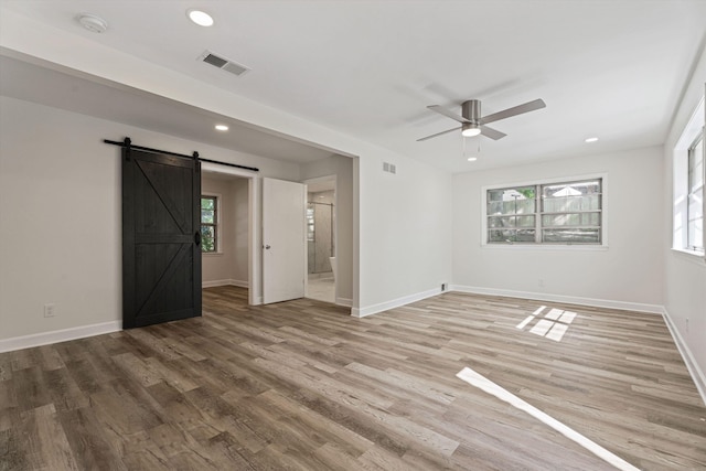 unfurnished room featuring light wood finished floors, visible vents, baseboards, and a barn door