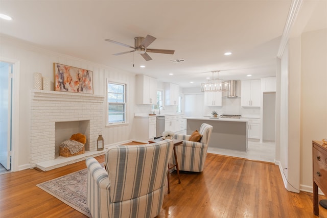 living room with visible vents, a brick fireplace, crown molding, and light wood-style floors