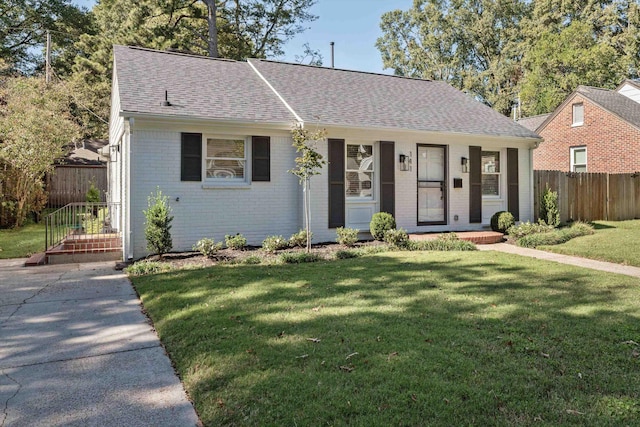 view of front of home with brick siding, a shingled roof, a front yard, and fence