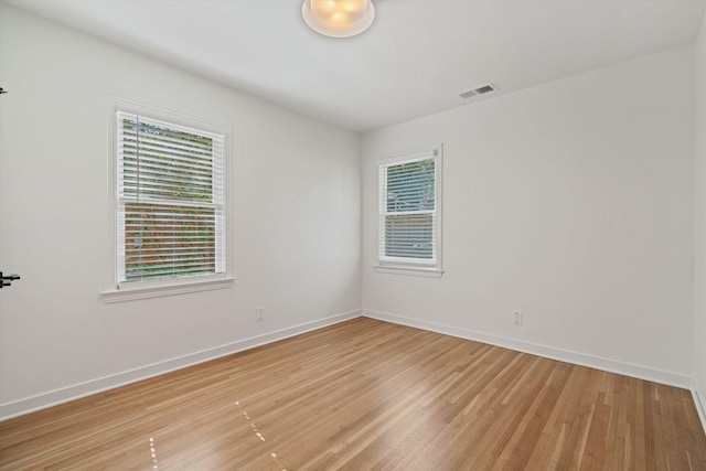 spare room with light wood-style flooring, baseboards, visible vents, and a wealth of natural light