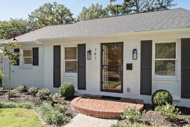 property entrance featuring brick siding and roof with shingles