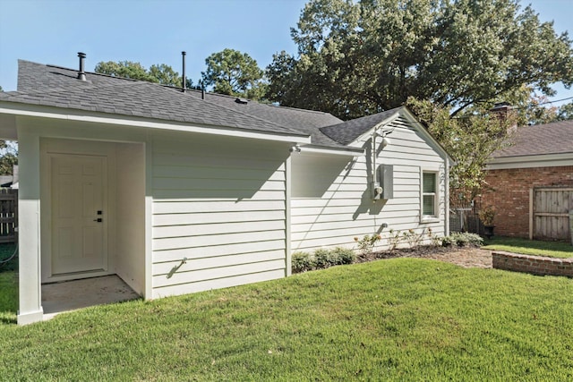 exterior space featuring a lawn, fence, and a shingled roof