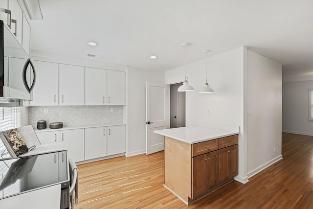 kitchen featuring visible vents, light wood-style flooring, decorative backsplash, white cabinets, and stainless steel microwave