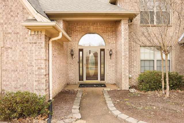 view of exterior entry featuring brick siding and roof with shingles