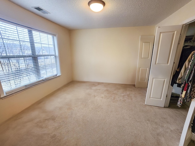 unfurnished bedroom with light carpet, visible vents, and a textured ceiling