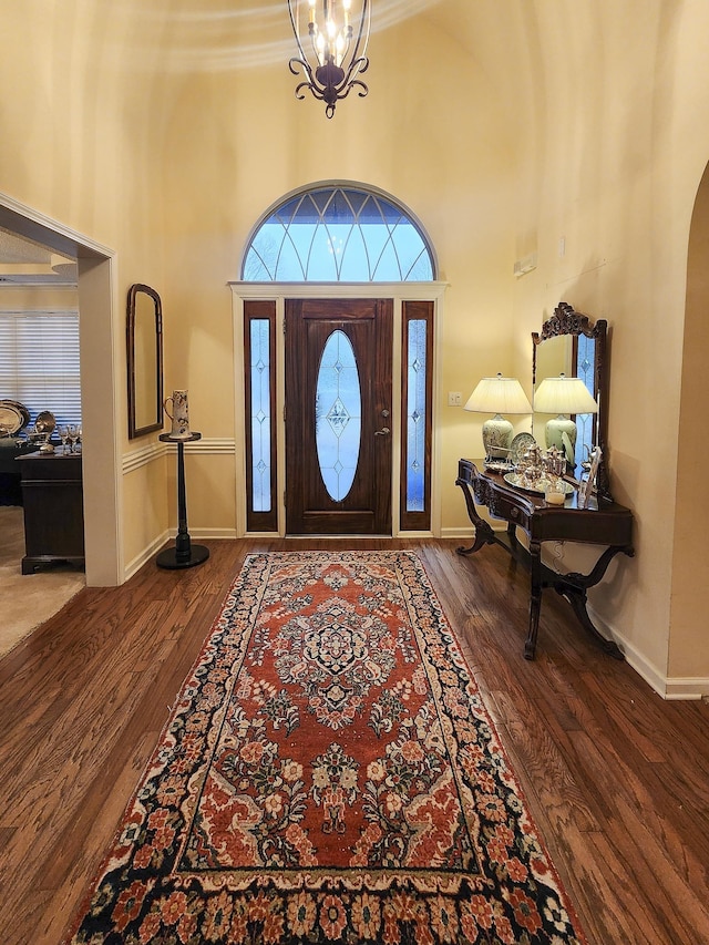 entryway featuring wood finished floors, a towering ceiling, arched walkways, baseboards, and a chandelier