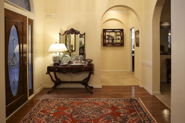 entryway with arched walkways, dark wood-style floors, and baseboards