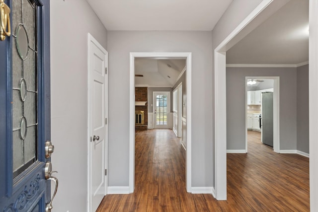 foyer featuring baseboards, a brick fireplace, dark wood-style floors, and crown molding