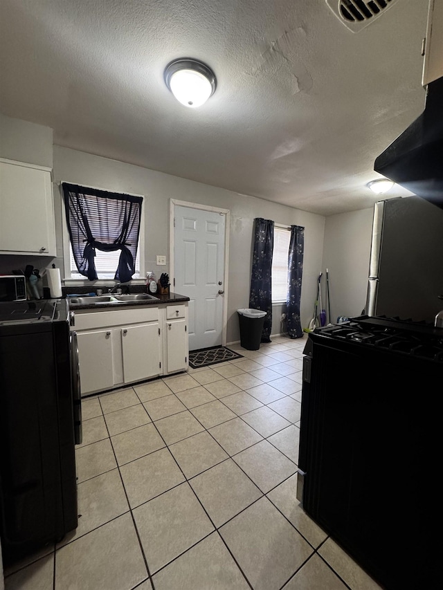 kitchen featuring visible vents, a sink, white cabinets, light tile patterned floors, and washer / dryer