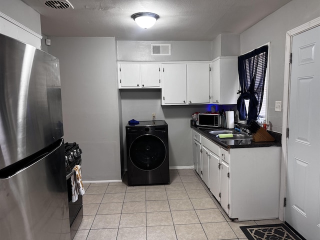 kitchen with visible vents, a sink, dark countertops, freestanding refrigerator, and washer / dryer