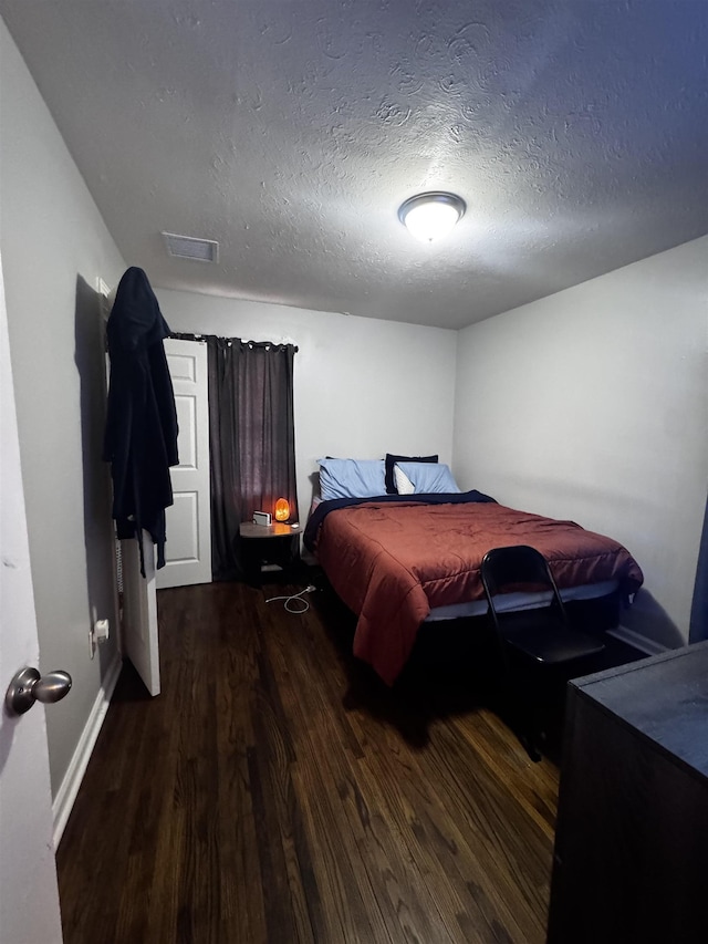 bedroom featuring visible vents, a textured ceiling, dark wood-type flooring, and baseboards