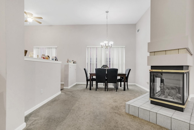 dining room with ceiling fan with notable chandelier, carpet flooring, baseboards, a towering ceiling, and a tile fireplace