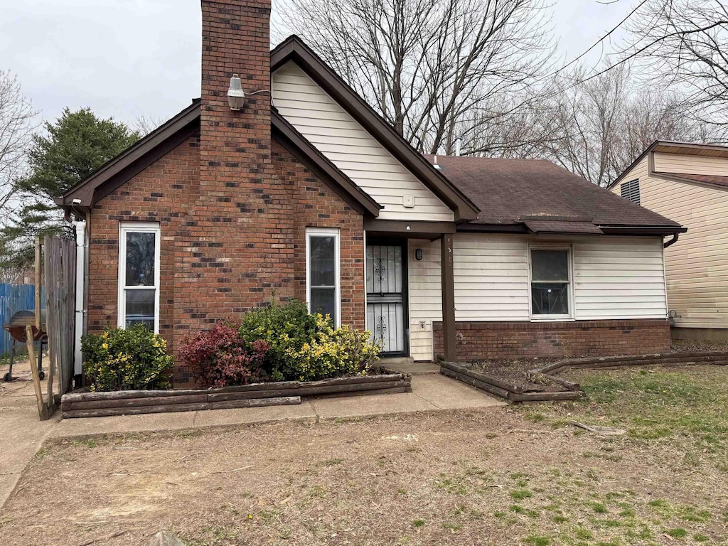 view of front of property with brick siding, a chimney, and a shingled roof