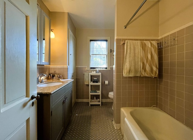 full bath with toilet, tile walls, wainscoting, tile patterned flooring, and vanity