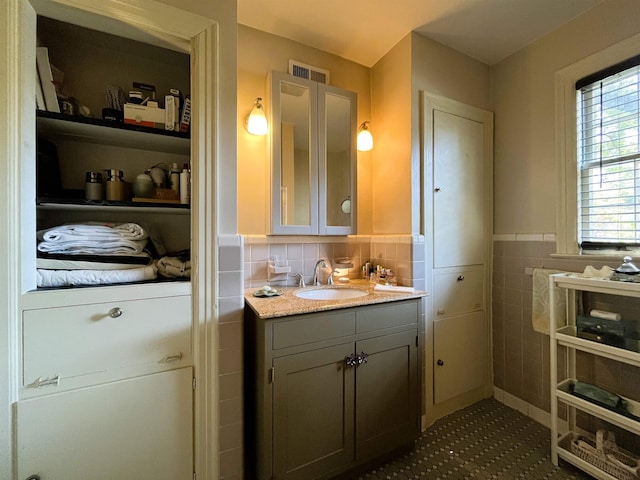 bathroom with visible vents, vanity, tile walls, and wainscoting