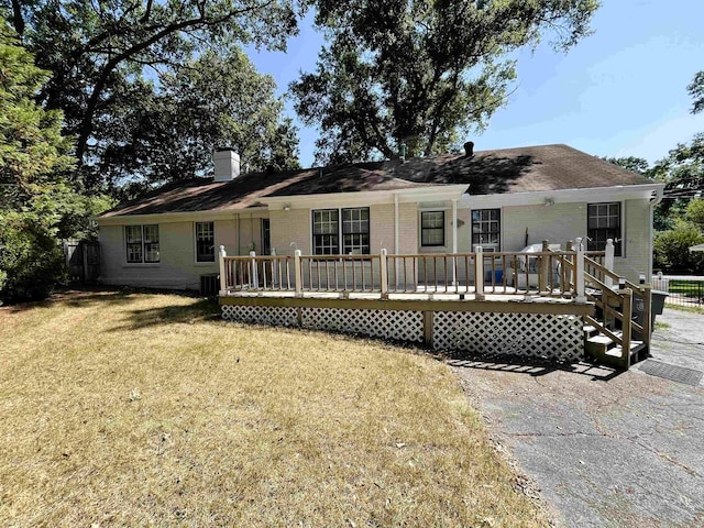 view of front of home featuring a wooden deck, a chimney, a front lawn, and brick siding