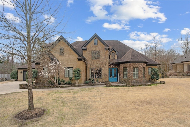 french country home featuring brick siding, french doors, a shingled roof, and a front yard