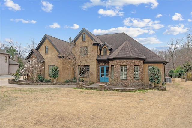 view of front of property with brick siding, roof with shingles, central AC, and fence