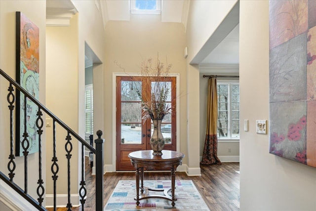 entryway with wood finished floors, crown molding, baseboards, a towering ceiling, and stairs