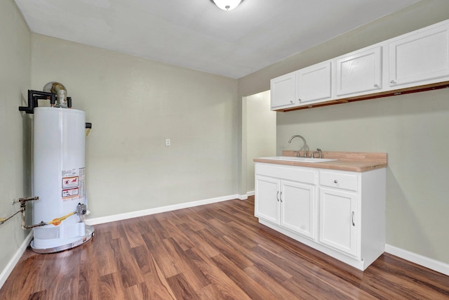 kitchen with baseboards, dark wood finished floors, water heater, white cabinetry, and a sink