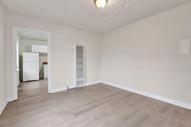 empty room featuring light wood finished floors, a heating unit, a textured ceiling, and baseboards