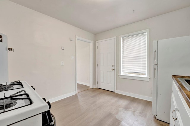 kitchen featuring baseboards, white appliances, and light wood finished floors