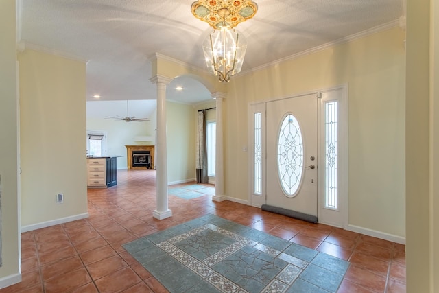 foyer featuring crown molding, decorative columns, a fireplace, and baseboards