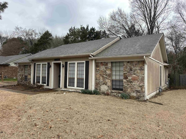 view of front of house with a front lawn, stone siding, and roof with shingles