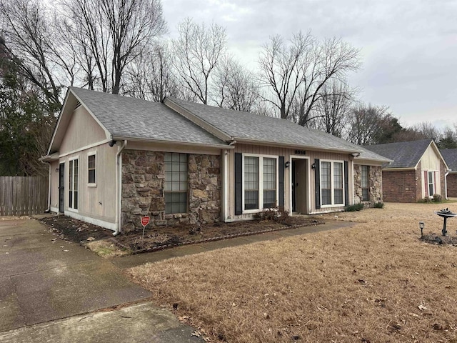 ranch-style house featuring fence, stone siding, and a shingled roof