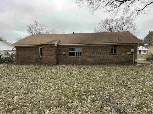 rear view of property featuring fence, a lawn, and brick siding