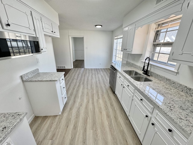 kitchen featuring light stone countertops, visible vents, stainless steel appliances, a sink, and light wood-type flooring