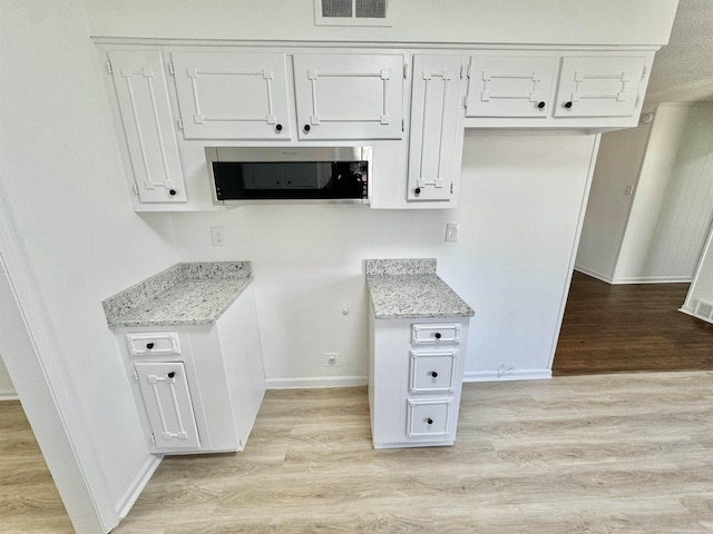 kitchen with light stone counters, stainless steel microwave, light wood-type flooring, and visible vents