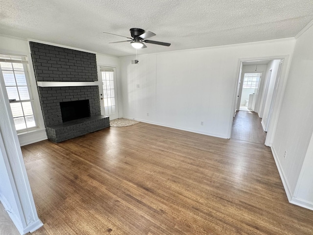 unfurnished living room with a brick fireplace, plenty of natural light, wood finished floors, and ornamental molding