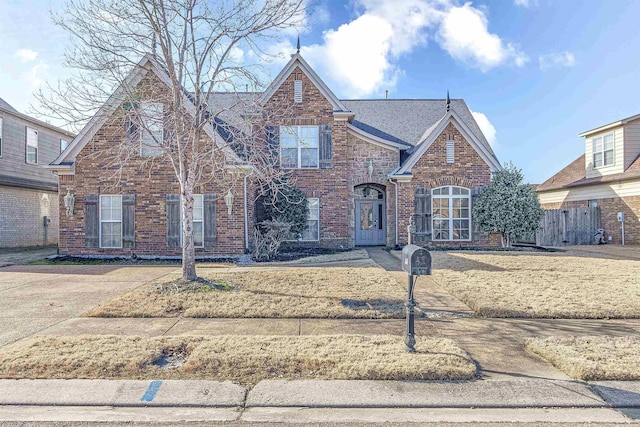 traditional home with brick siding, roof with shingles, and fence