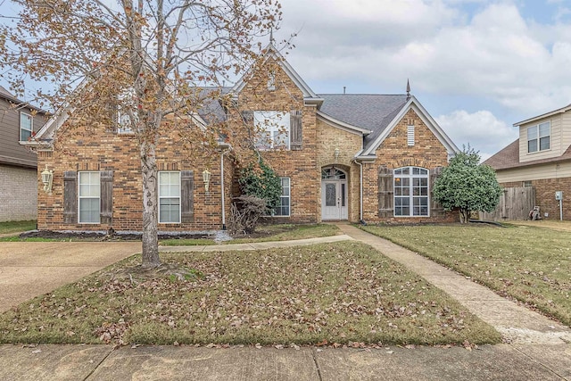 traditional-style home with brick siding, a front lawn, and roof with shingles