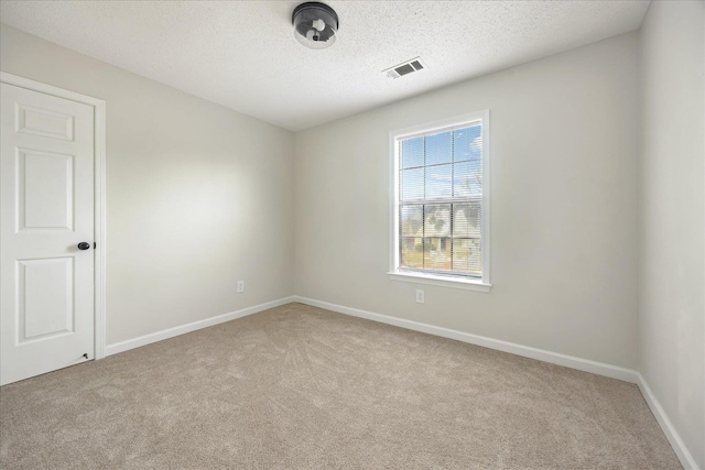 empty room with carpet flooring, baseboards, visible vents, and a textured ceiling