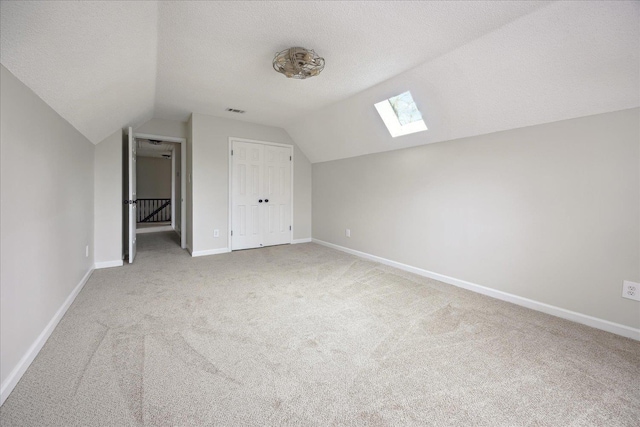 additional living space with visible vents, baseboards, lofted ceiling with skylight, carpet flooring, and a textured ceiling