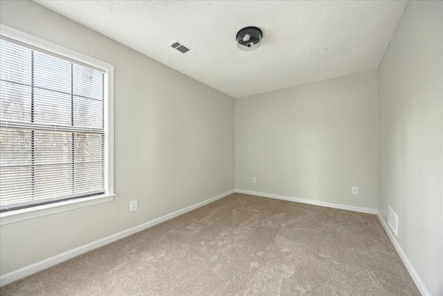 unfurnished room with a textured ceiling, baseboards, visible vents, and light carpet