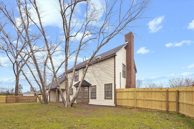 rear view of property featuring a lawn, a chimney, and fence