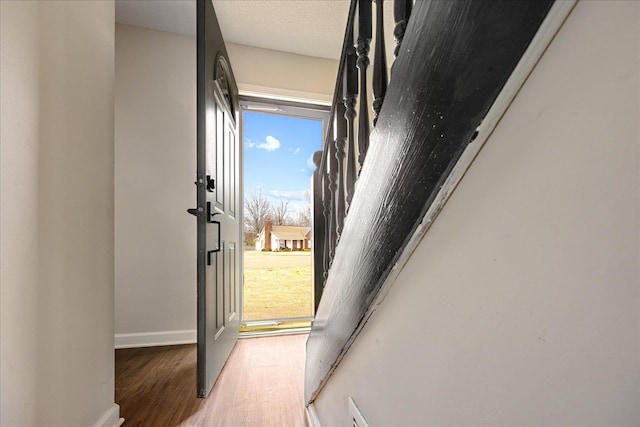 doorway to outside with visible vents, baseboards, a textured ceiling, and wood finished floors