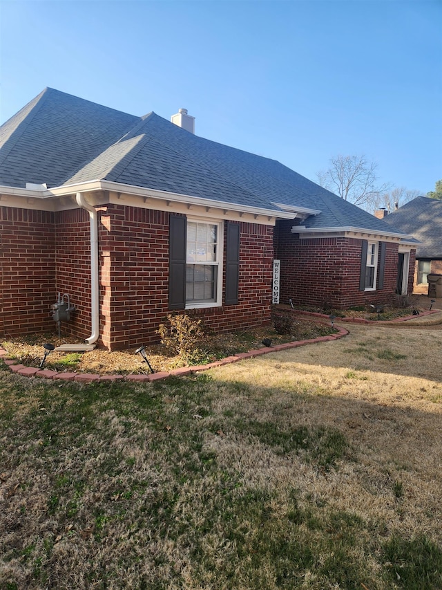 view of property exterior with brick siding, a chimney, a yard, and a shingled roof